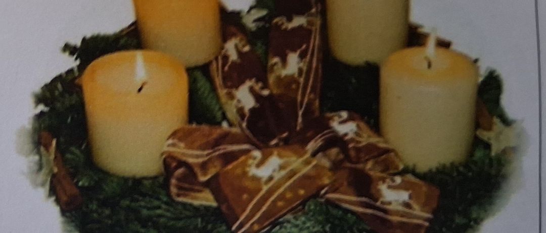 Vier Kerzen sind in einem Kreis angeordnet, möglicherweise für einen Adventskranz, geschmückt mit grünen Blättern und einem braunen Band mit weißen Designs.