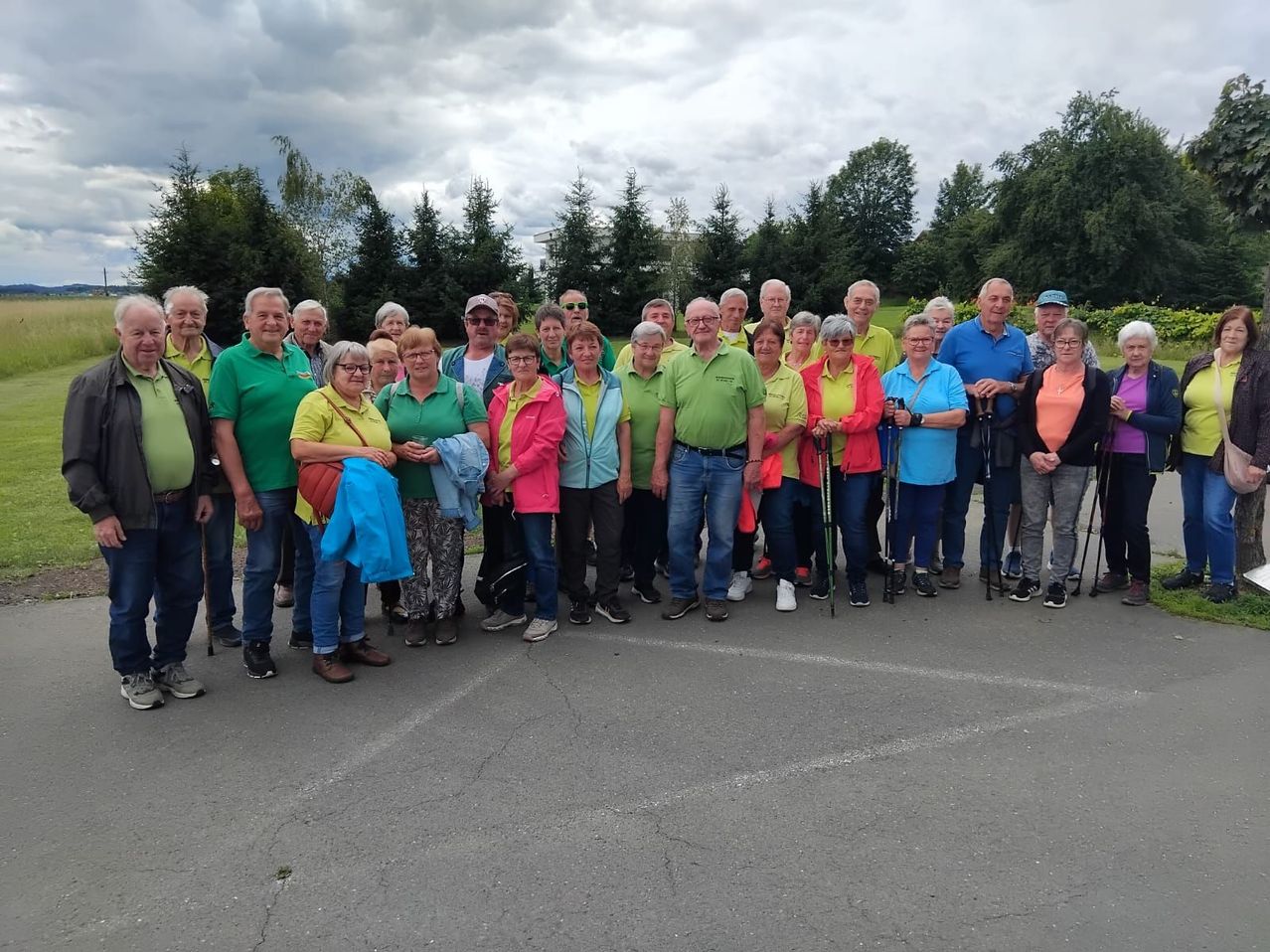 A group of people dressed in various colored shirts and pants pose for a photo on a paved road with trees in the background.