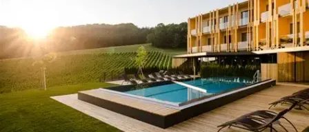 Ein Resort mit einer hölzernen Poolterrasse, Liegestühlen und einem gelben Gebäude gegen einen untergehenden Sonnenschein.