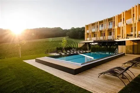 Ein Resort mit einer hölzernen Poolterrasse, Liegestühlen und einem gelben Gebäude gegen einen untergehenden Sonnenschein.