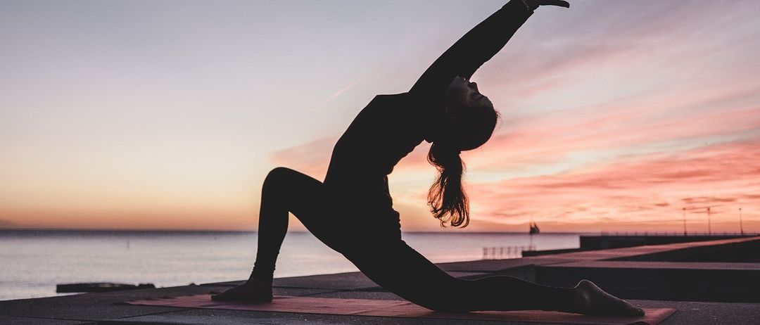 Die Silhouette einer Frau, die Yoga-Posen am Meer während eines Sonnenuntergangs praktiziert.