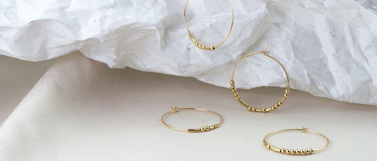 Vier goldene Creolen in verschiedenen Größen und Mustern mit Perlen sind auf einem weißen Stoffhintergrund ausgestellt.