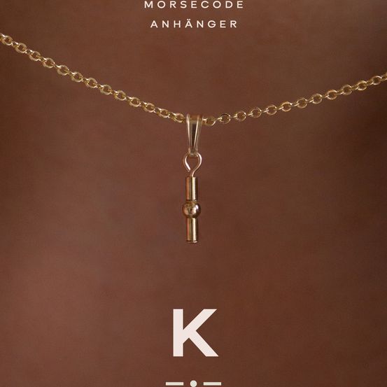 Eine goldene Kette mit einem Morse-Code-Anhänger in Form eines Schlüssels hängt auf einem braunen Hintergrund. Der Anhänger zeigt 'K'.