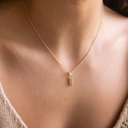 Eine Frau trägt eine goldene Halskette mit einem kleinen Anhänger auf ihrer Brust.