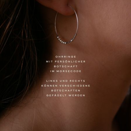 Nahaufnahme einer Frauenohr mit einem silbernen Creolen-Ohrring, verziert mit kleinen Perlen. Der Textüberlagerung steht 'Ohrring mit persönlicher Botschaft im Morsecode.'