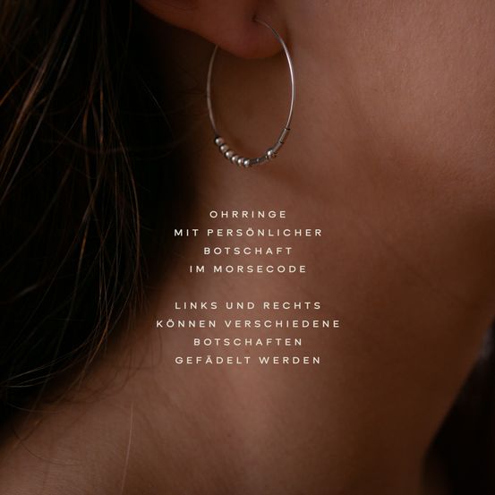 Nahaufnahme einer Frauenohr mit einem silbernen Creolen-Ohrring, verziert mit kleinen Perlen. Der Textüberlagerung steht 'Ohrring mit persönlicher Botschaft im Morsecode.'