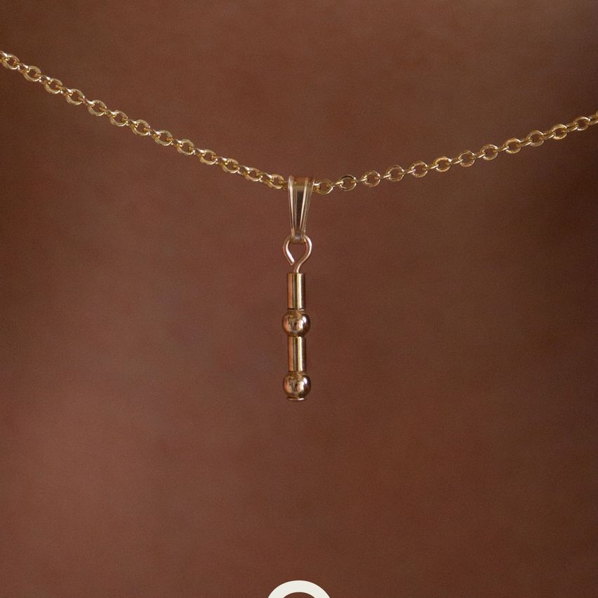 Eine goldene Kettenkette mit einem kleinen Anhänger auf einem braunen Hintergrund. Der Anhänger besteht aus drei goldenen Perlen.