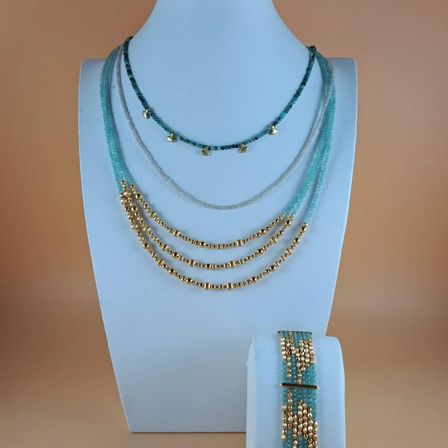 Eine Präsentation von mehrreihigen Halsketten mit türkisfarbenen und goldenen Perlen auf einem weißen Mannequin. Ein passendes Armband wird rechts daneben ausgestellt.