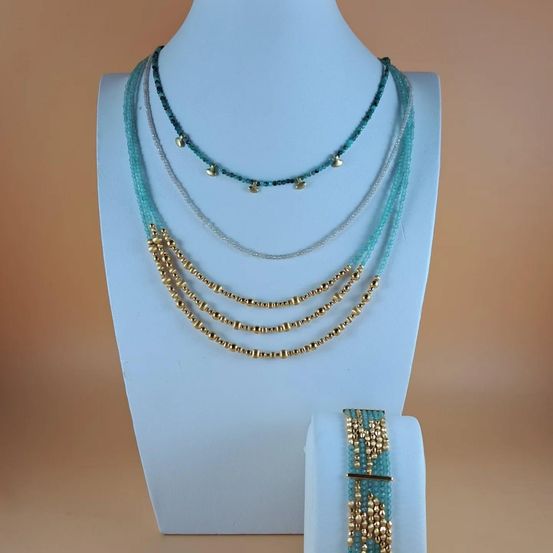 Eine Präsentation von mehrreihigen Halsketten mit türkisfarbenen und goldenen Perlen auf einem weißen Mannequin. Ein passendes Armband wird rechts daneben ausgestellt.