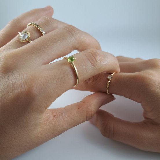Die Hände einer Person zeigen einen goldenen Ring mit einem grünen Stein und einen goldenen Ring mit einer Perle an der linken Hand.