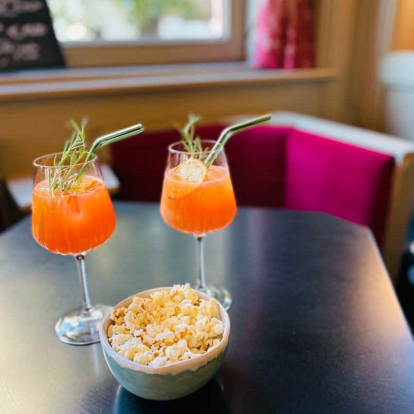Zwei orange Getränke in Gläsern mit Strohhalmen und eine Schüssel Popcorn auf einem Tisch.