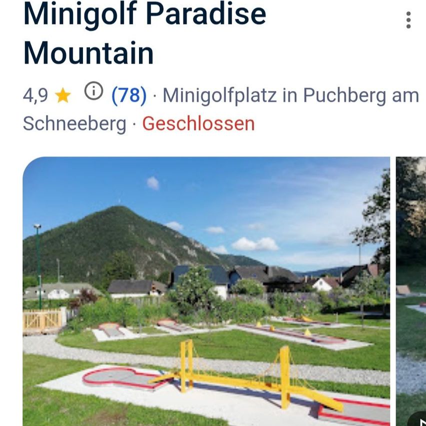 Minigolf Paradise Mountain zeigt einen Minigolfplatz mit einer gelben Brücke und einem Berg im Hintergrund. Der Platz ist von grünem Rasen umgeben und hat mehrere Löcher.