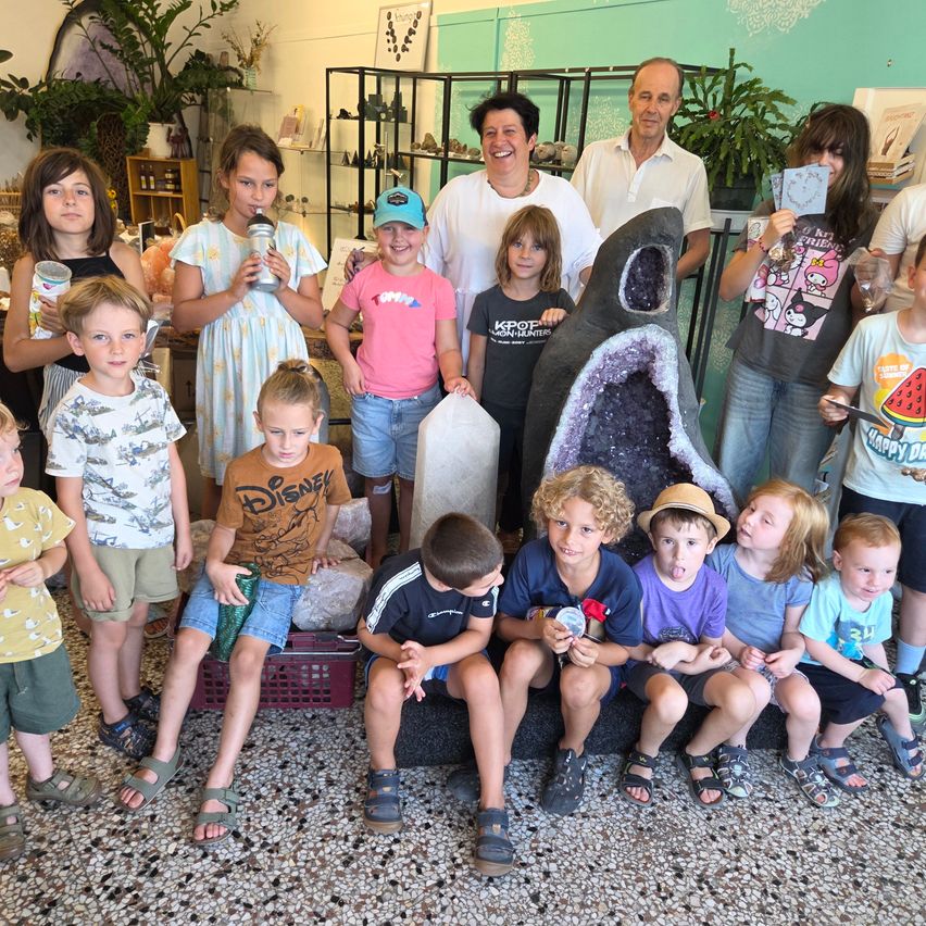 Eine Gruppe von Kindern und Erwachsenen posiert für ein Foto in einem Raum mit einem großen Kristall und Pflanzen im Hintergrund.