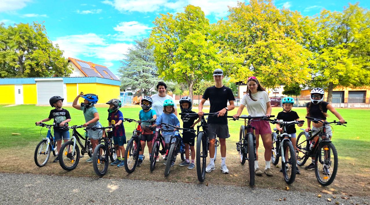 Eine Gruppe von Kindern und Erwachsenen steht mit ihren Fahrrädern in einem Park und lächelt für ein Foto.