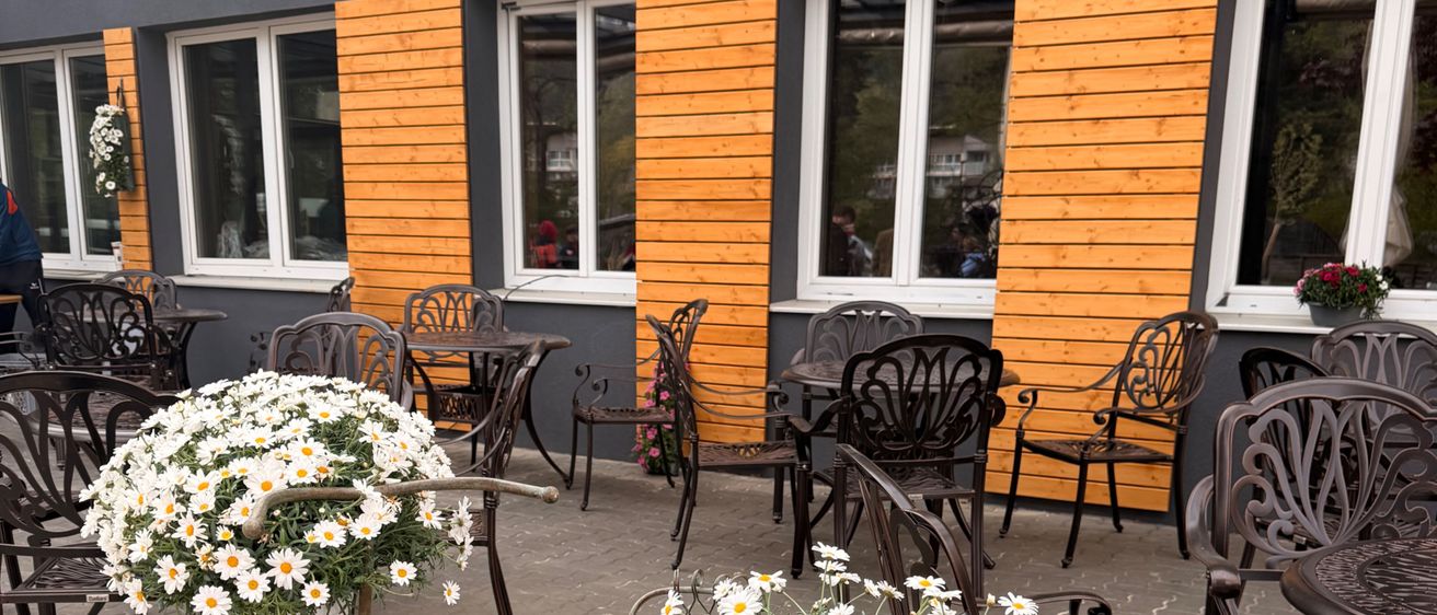 Ein Außensitzbereich mit einem Fahrraddekor, gefüllt mit weißen und lila Blumen. Holzverkleidungen und weiße Fenster schmücken das Gebäude dahinter.