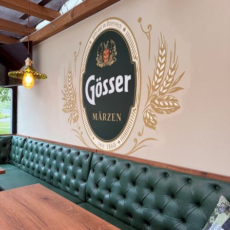 Ein Restaurant mit einer grünen Lederbank und einer Wand mit einem Gösser Logo mit einem goldenen Weizendesign.