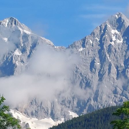Berge mit Nebel an einem sonnigen Tag. Die Gipfel sind felsige und schneebedeckt.