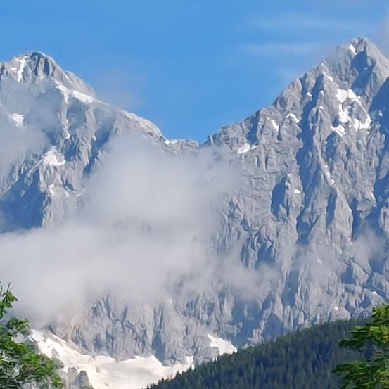 Berge mit Nebel an einem sonnigen Tag. Die Gipfel sind felsige und schneebedeckt.
