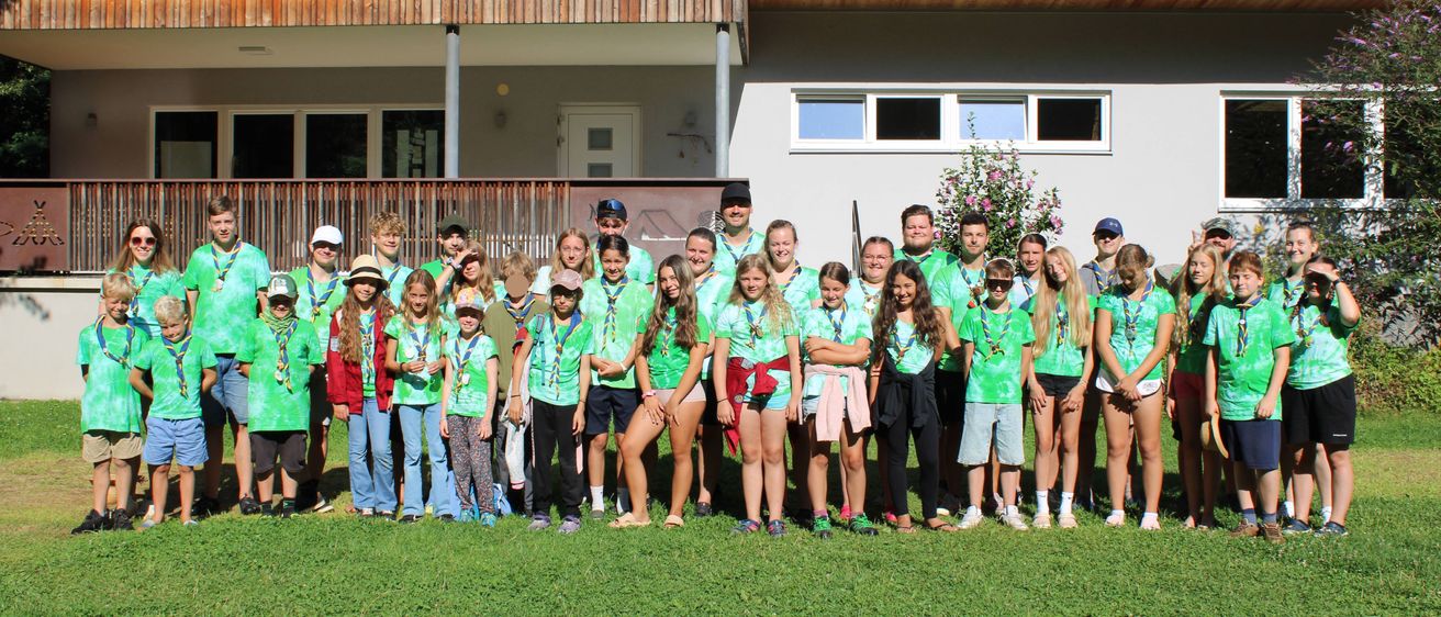 Eine Gruppe junger Menschen in grünen Shirts und Shorts steht vor einem Haus. Sie lächeln und scheinen für ein Foto zu posieren.
