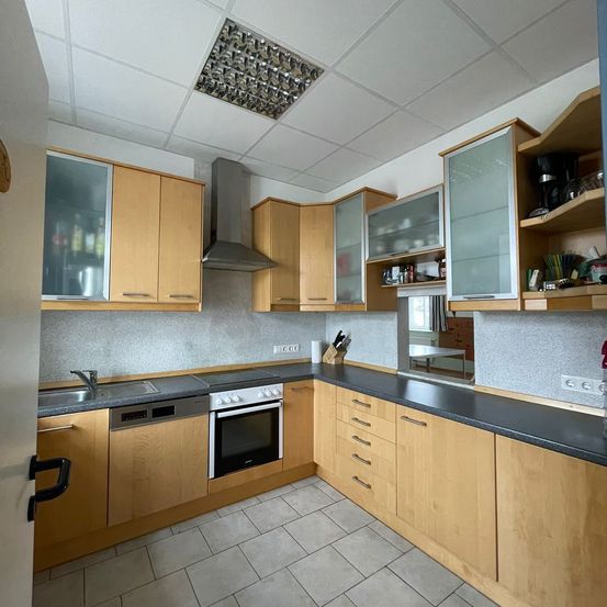 Eine moderne Küche mit Holzschränken, schwarzen Arbeitsplatten und Edelstahlgeräten. Die Decke hat ein Metallgitter. Es gibt einen Geschirrspüler, einen Ofen und einen Herd.