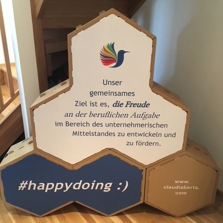 Eine sechseckige Schachtel mit einem Vogel auf der Oberseite, es steht: Unser gemeinsames Ziel ist es, die Freude an der beruflichen Aufgabe zu entwickeln und zu fördern. #happydoing :) www.claudiaberta.com.