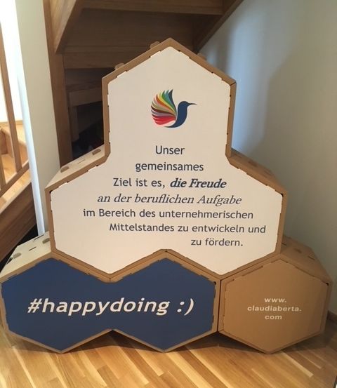 Eine sechseckige Schachtel mit einem Vogel auf der Oberseite, es steht: Unser gemeinsames Ziel ist es, die Freude an der beruflichen Aufgabe zu entwickeln und zu fördern. #happydoing :) www.claudiaberta.com.
