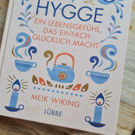 Ein Buch mit dem Titel 'Hygge' von Meik Wiking, mit Illustrationen von Teetassen, Teekannen und Kerzen.
