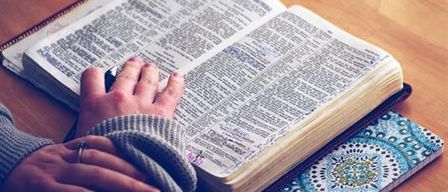 Eine Person liest ein Buch auf einem Holztisch mit einem dekorativen Notizbuch darunter.