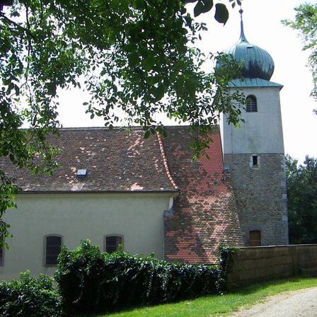 Eine historische Kirche mit einem roten Dach und einem hohen Turm mit einer grünen Kuppel. Der Turm hat ein kleines Fenster an der Seite.
