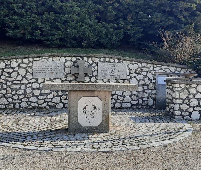 Ein Steinaltar mit Kreuz und Tafeln ist von Cobblestones umgeben. Bäume und Büsche sind im Hintergrund.
