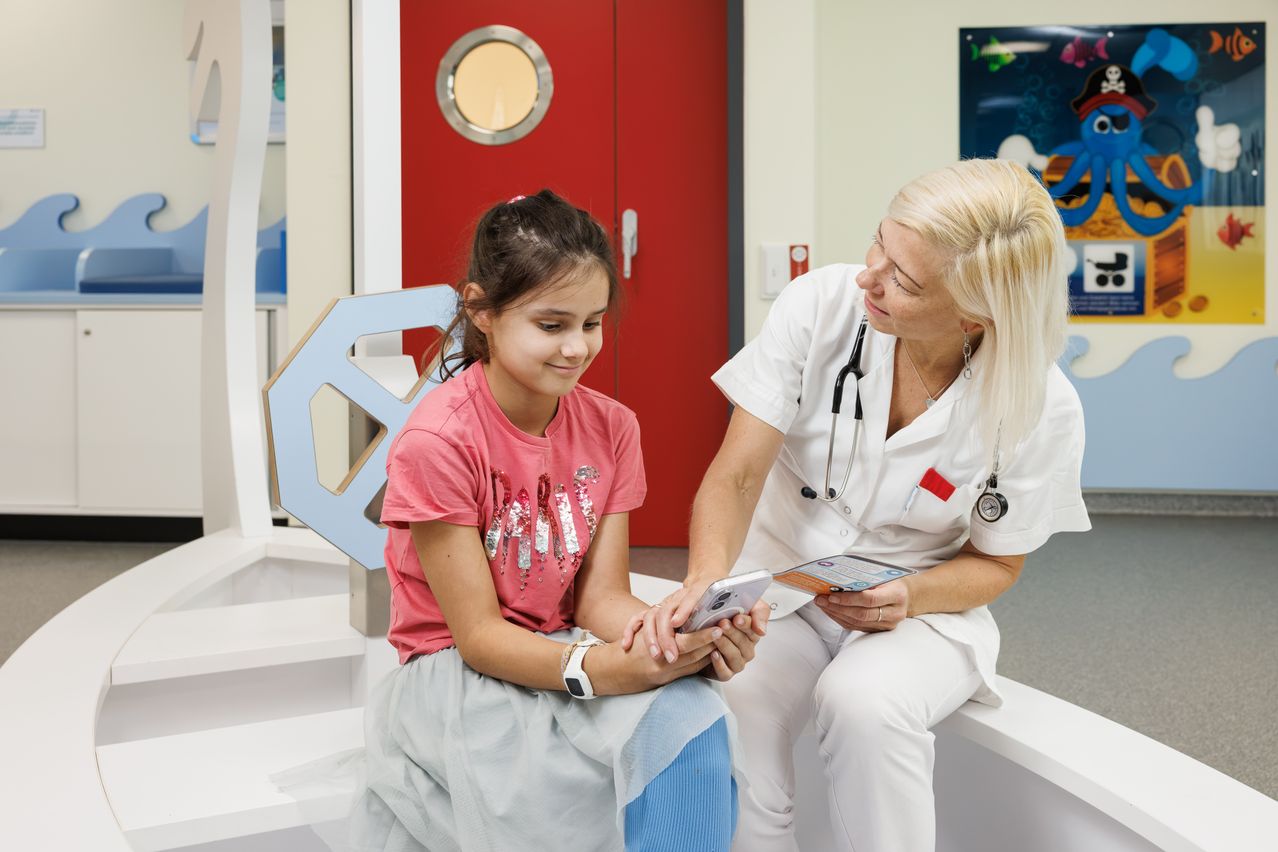 Ein junges Mädchen mit einem rosa T-Shirt schaut sich mit einer Krankenschwester in einem Krankenhauszimmer ein Tablet an.
