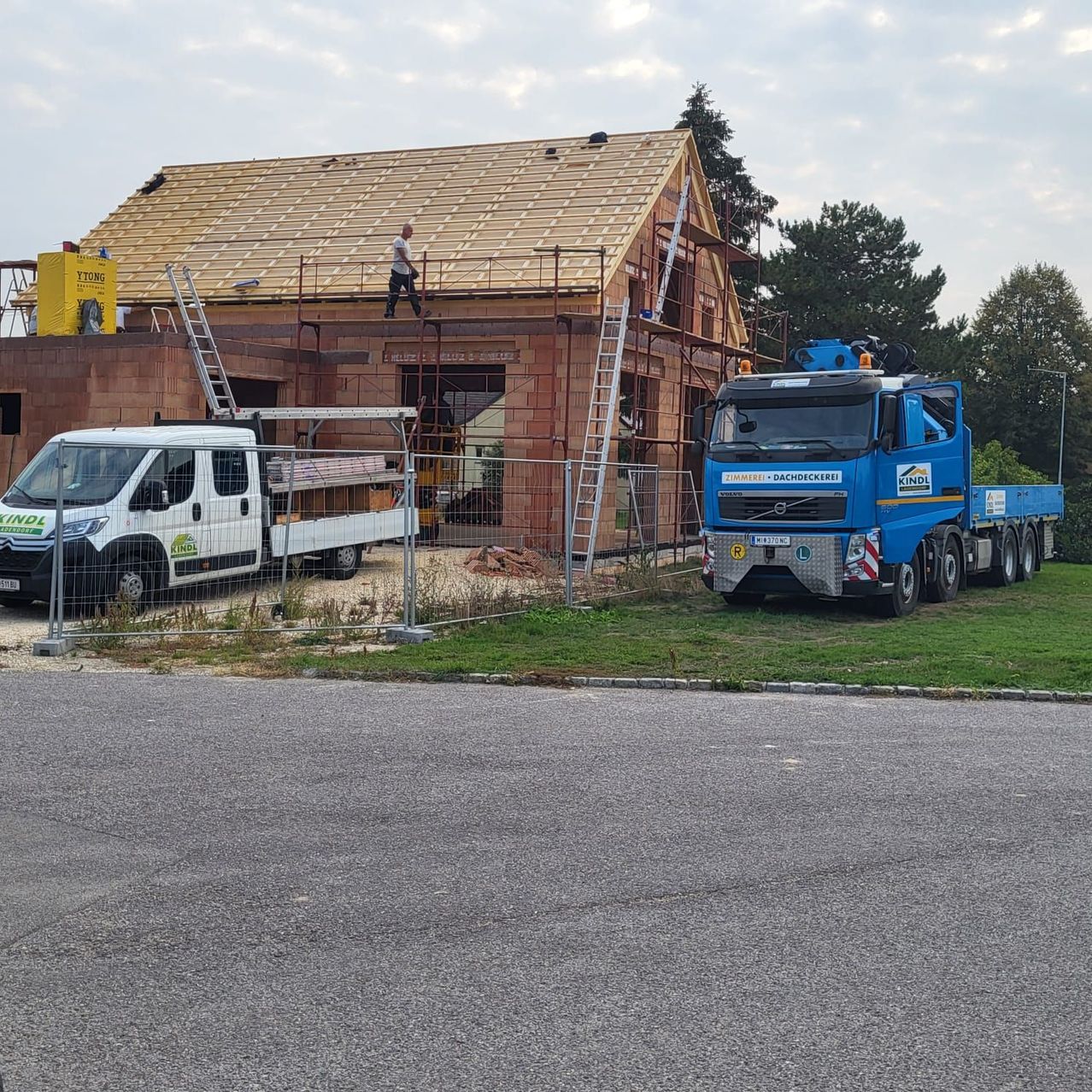 Ein Haus im Bau mit einem neuen Dach. Ein Mann steht auf dem Dach und ein Lastwagen ist in der Nähe geparkt.