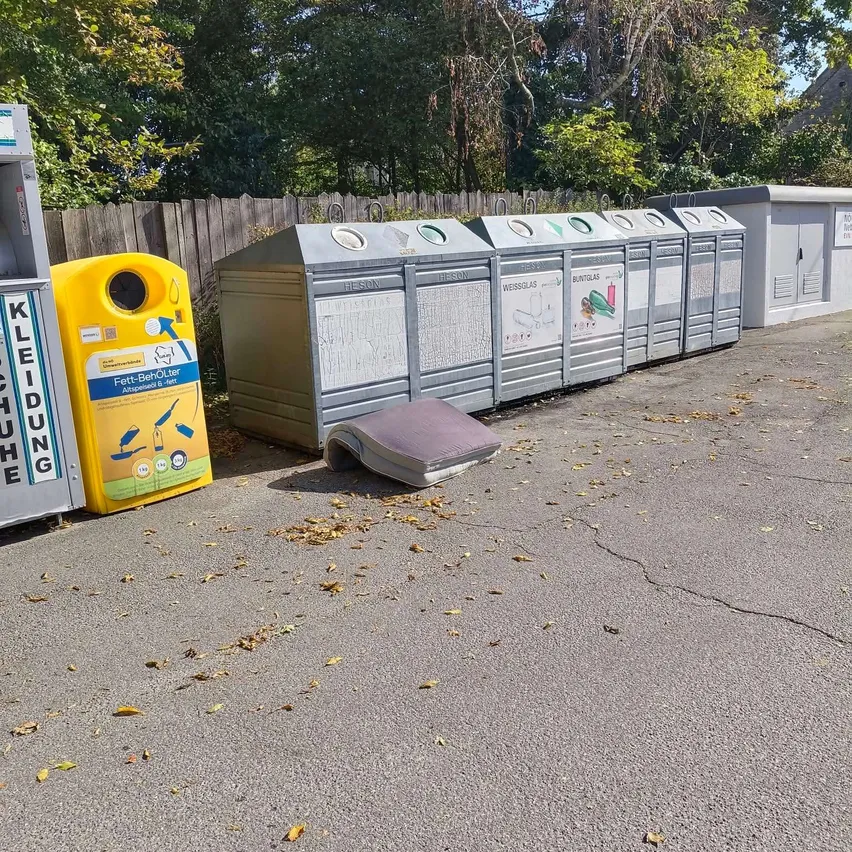 Eine Reihe von grauen Recyclingbehältern mit einem gelben Behälter auf der linken Seite und einem umgefallenen grauen Behälter auf dem Boden.