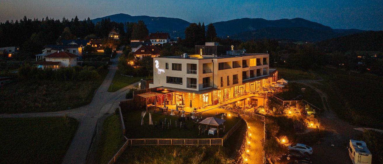 Auf einem Hügel leuchtet ein modernes Hotel mit warmen Lichtern vor einer Kulisse aus Bergen und einem klaren Nachthimmel.
