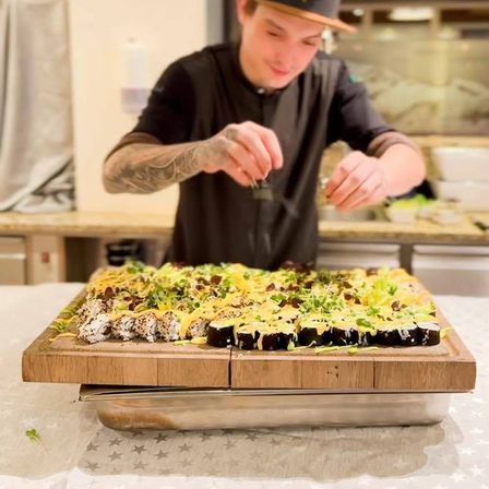 Ein Koch bereitet eine Sushi-Platte auf einem Holzbrett in einer Küche zu und verfeinert sie.