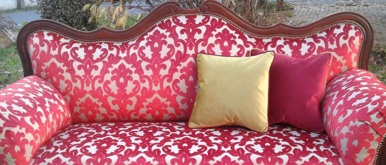 Ein vintage rotes und weißes gemustertes Sofa mit hölzerne Rahmen und zwei Kissen, eines gelb und eines rot, auf einer grauen Betonfläche.