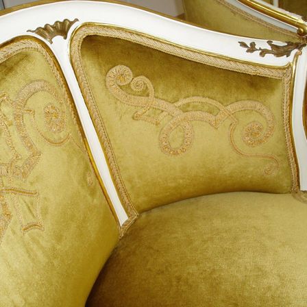 Nahaufnahme eines luxuriösen Sofas mit Gold-Samt-Polsterung, weißer und goldener Einfassung und aufwendigen gestickten Mustern.
