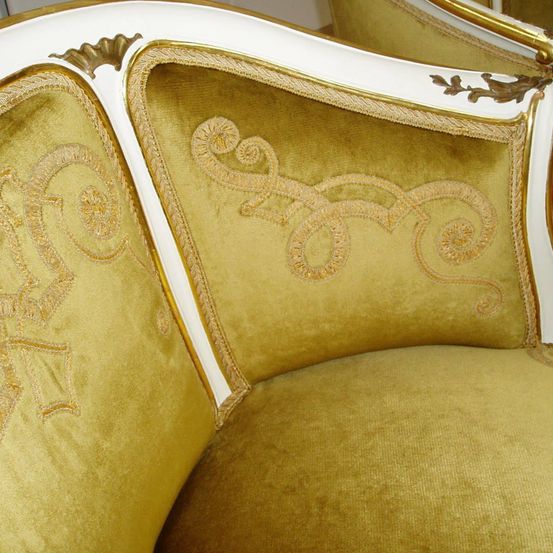 Nahaufnahme eines luxuriösen Sofas mit Gold-Samt-Polsterung, weißer und goldener Einfassung und aufwendigen gestickten Mustern.