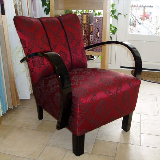 Ein roter Sessel mit aufwendigen Mustern und schwarzen Armlehnen steht auf einem gefliesten Boden vor einer Glastür.