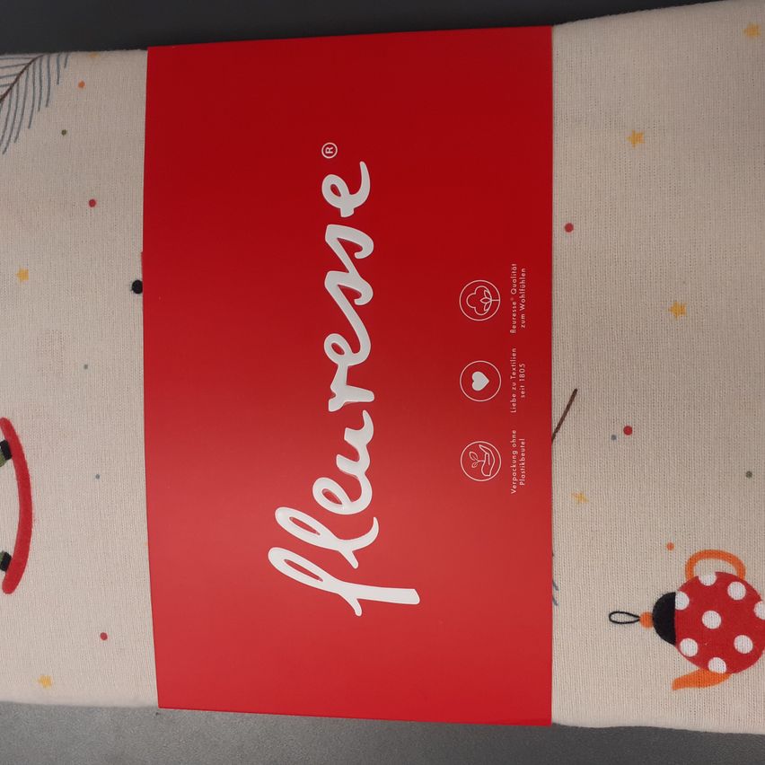 Ein rotes und weißes Paket Babybettwäsche mit einem Punktmuster. Es hat das Wort 'Pleurer' in weiß geschrieben. Auf der rechten Seite gibt es ein rotes und weißes Punktmuster.