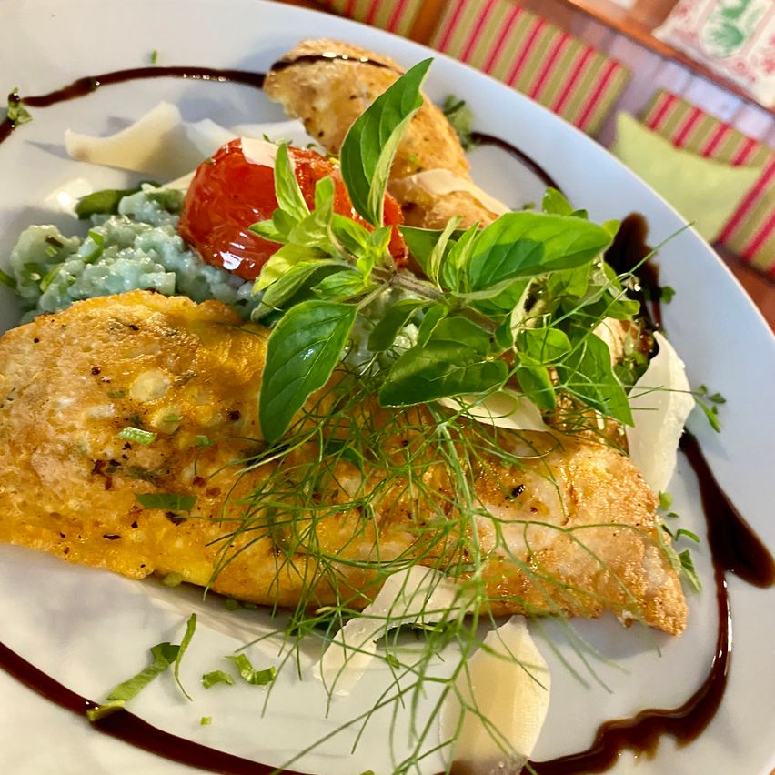 A plate with a golden fried fish fillet, garnished with green herbs, a slice of tomato, and a drizzle of sauce.