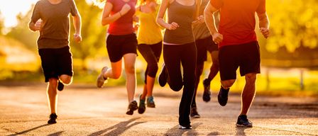 Eine Gruppe von Menschen joggt auf einem Pfad, umgeben von Bäumen. Sie sind in Trainingskleidung gekleidet.