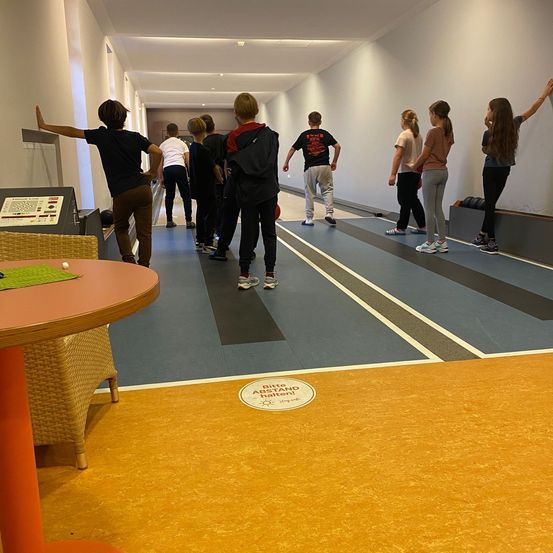 Eine Gruppe von Menschen läuft auf einer Bowlingbahn mit weißen und grauen Markierungen. Eine Person hebt die Hand.