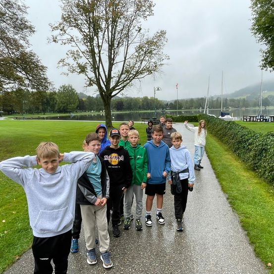 Eine Gruppe von Kindern steht auf einem Weg, möglicherweise in einem Park. Sie lächeln und posieren für ein Foto.
