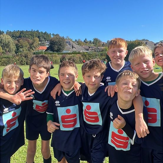 Eine Gruppe von Jungen in identischen Fußballtrikots posiert für ein Foto an einem sonnigen Tag.