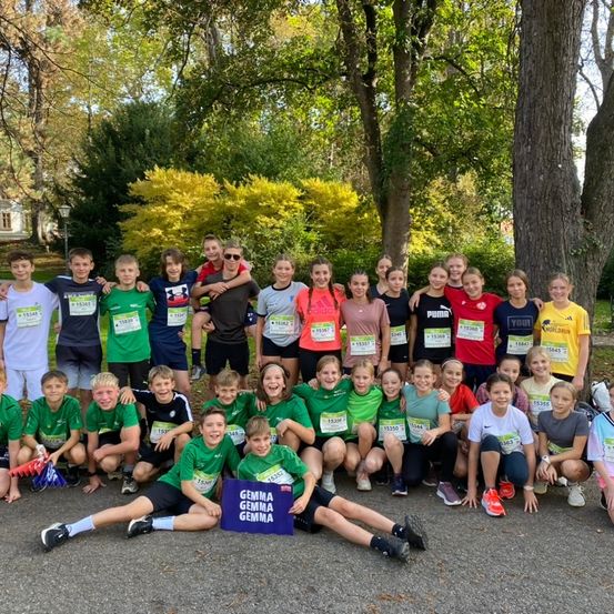 Eine Gruppe von Kindern und Erwachsenen posiert für ein Foto im Park. Sie tragen Startnummern für einen Lauf.