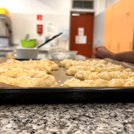 Ein Backblech mit goldenbraunen, mit Zucker bestreuten Brötchen liegt auf einer Granitarbeitsplatte in einer Küche. Im Hintergrund ist eine verschwommene Tür und Schränke zu sehen.