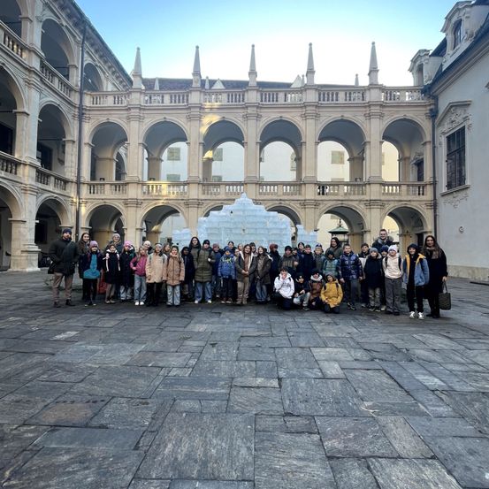 Eine Gruppe von Menschen posiert für ein Foto vor einem historischen Gebäude mit Bogenfenstern und einer Schneeskulptur in der Mitte.