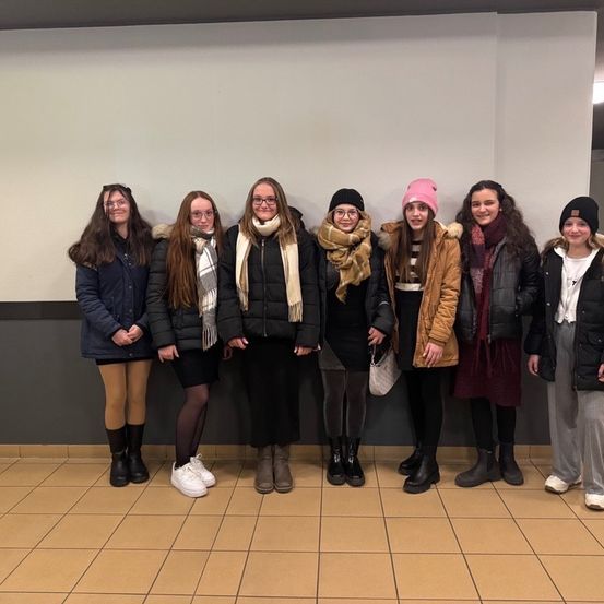 Eine Gruppe junger Frauen, in Winterkleidung gekleidet, steht lächelnd für ein Foto in einem Flur.