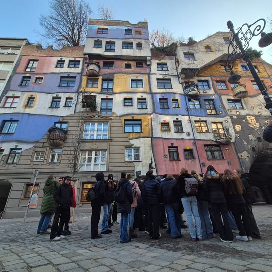 Eine Gruppe von Menschen steht vor einem lebhaft bemalten Gebäude mit Balkonen und Fenstern, unter einem klaren Himmel.